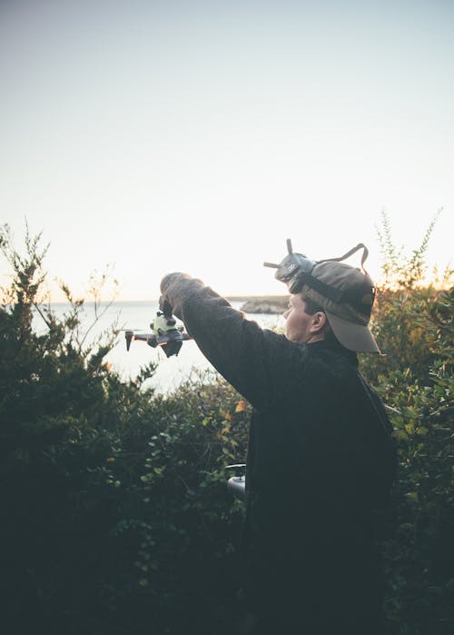 Man with Drone Standing by Bushes on Sea Coast at Sunset