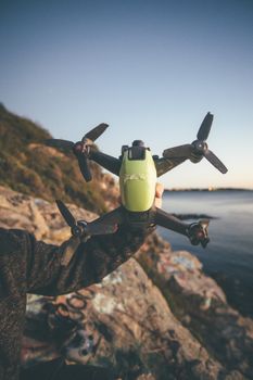 A close-up of a hand holding a drone with propellers, taken outdoors near a rocky coastline.