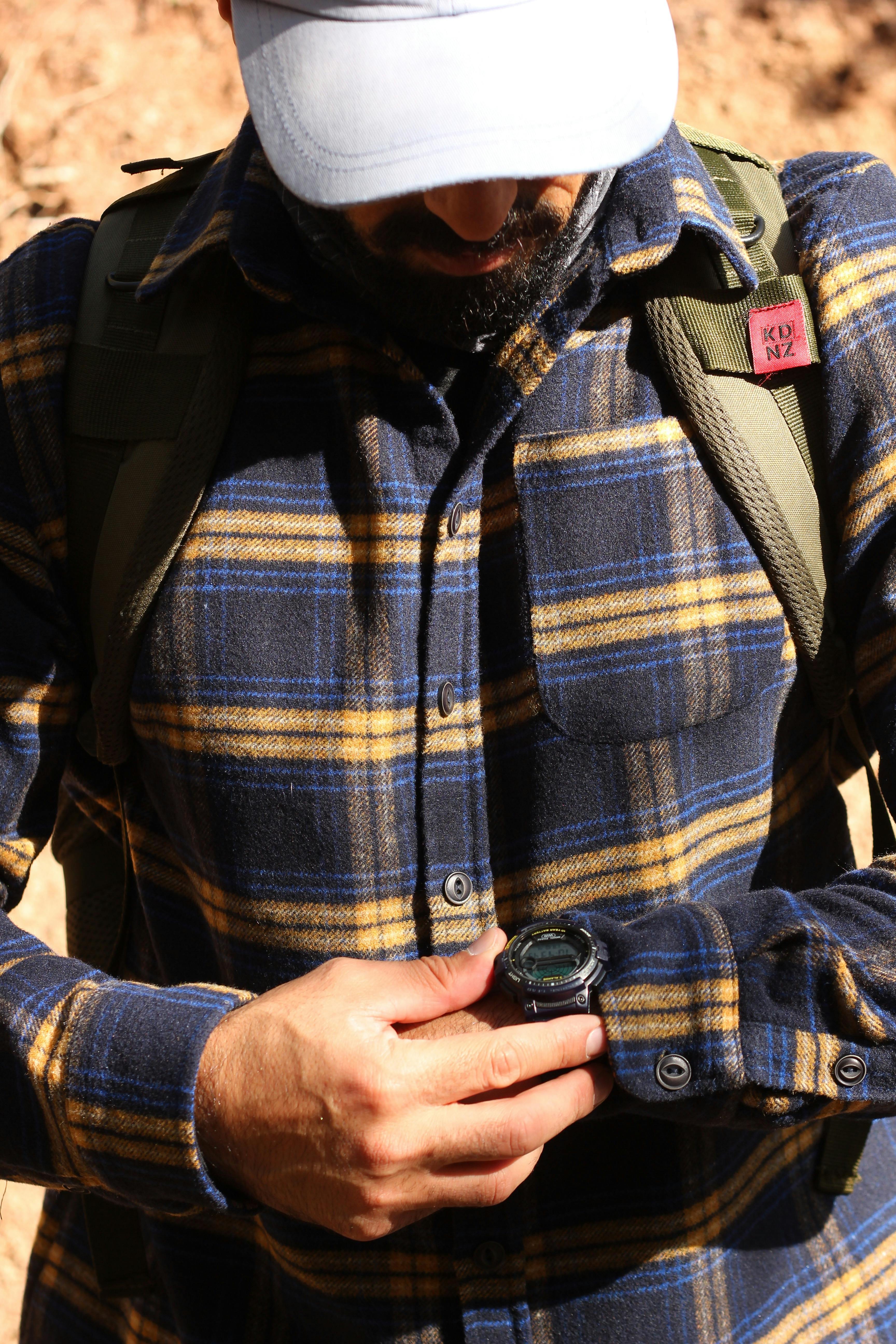 Close-up of a man outdoors checking his wristwatch, dressed for a hike.
