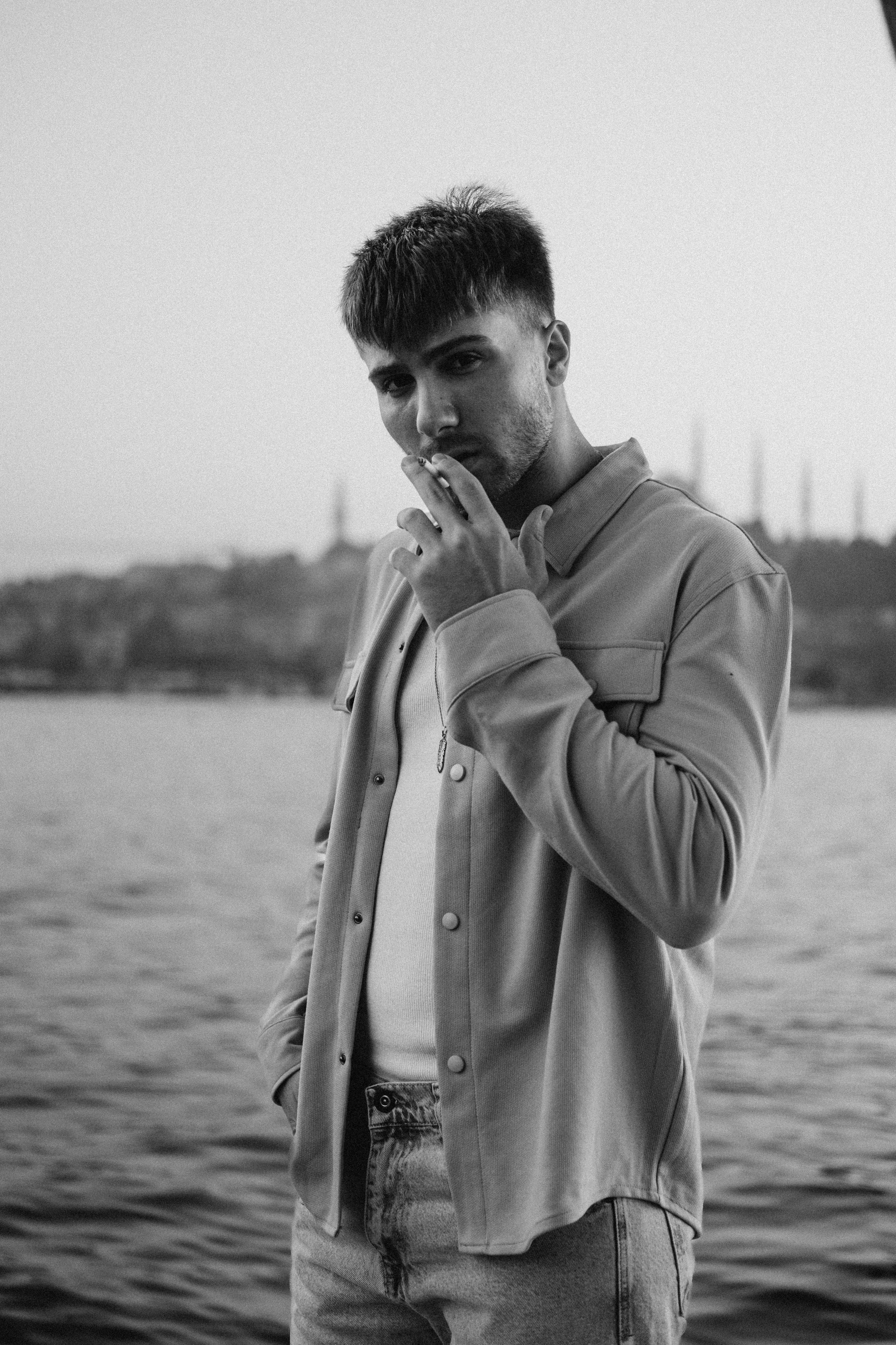 A fashionable man poses by the Bosphorus in Istanbul, embodying modern urban style.