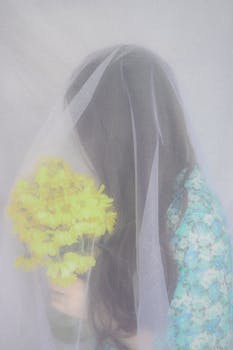 Artistic portrait of a bride with a bouquet under a soft veil, exuding dreamy elegance.