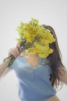 Woman in a blue shirt holding a bouquet of yellow flowers against a light background.