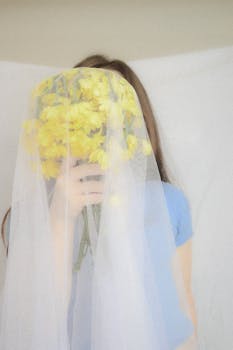 Artistic portrait of a young woman with yellow flowers under a veil, creating a dreamy atmosphere.