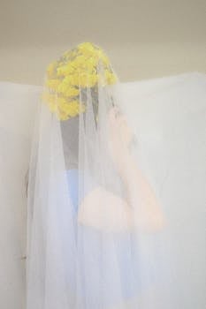 Stylized bridal portrait featuring a woman with a tulle veil and bouquet, captured in soft pastels indoors.