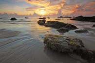 宁静的海滩日出场景中，岩石与海浪交织出令人惊叹的景色