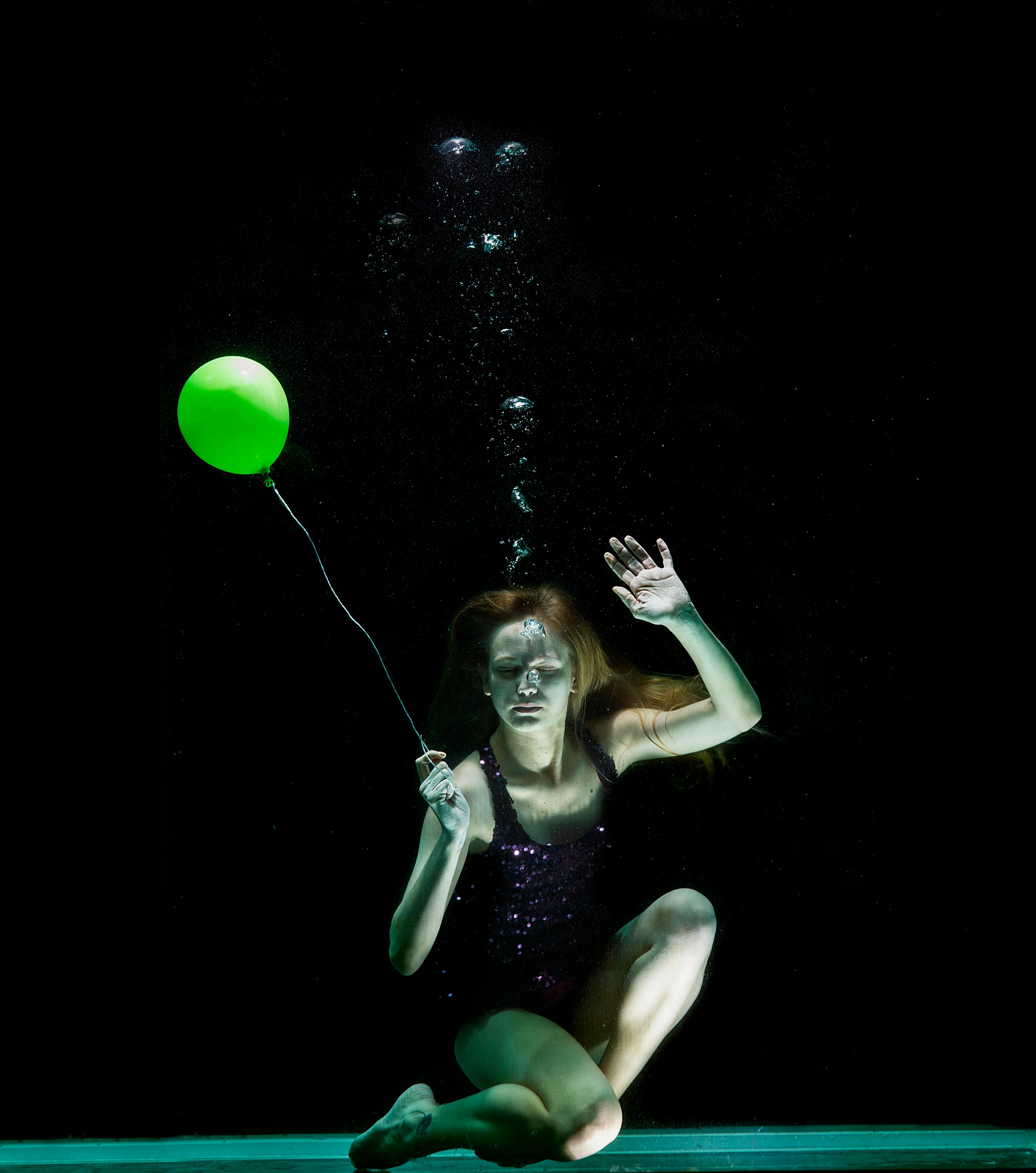 underwater photography of woman holding green balloon