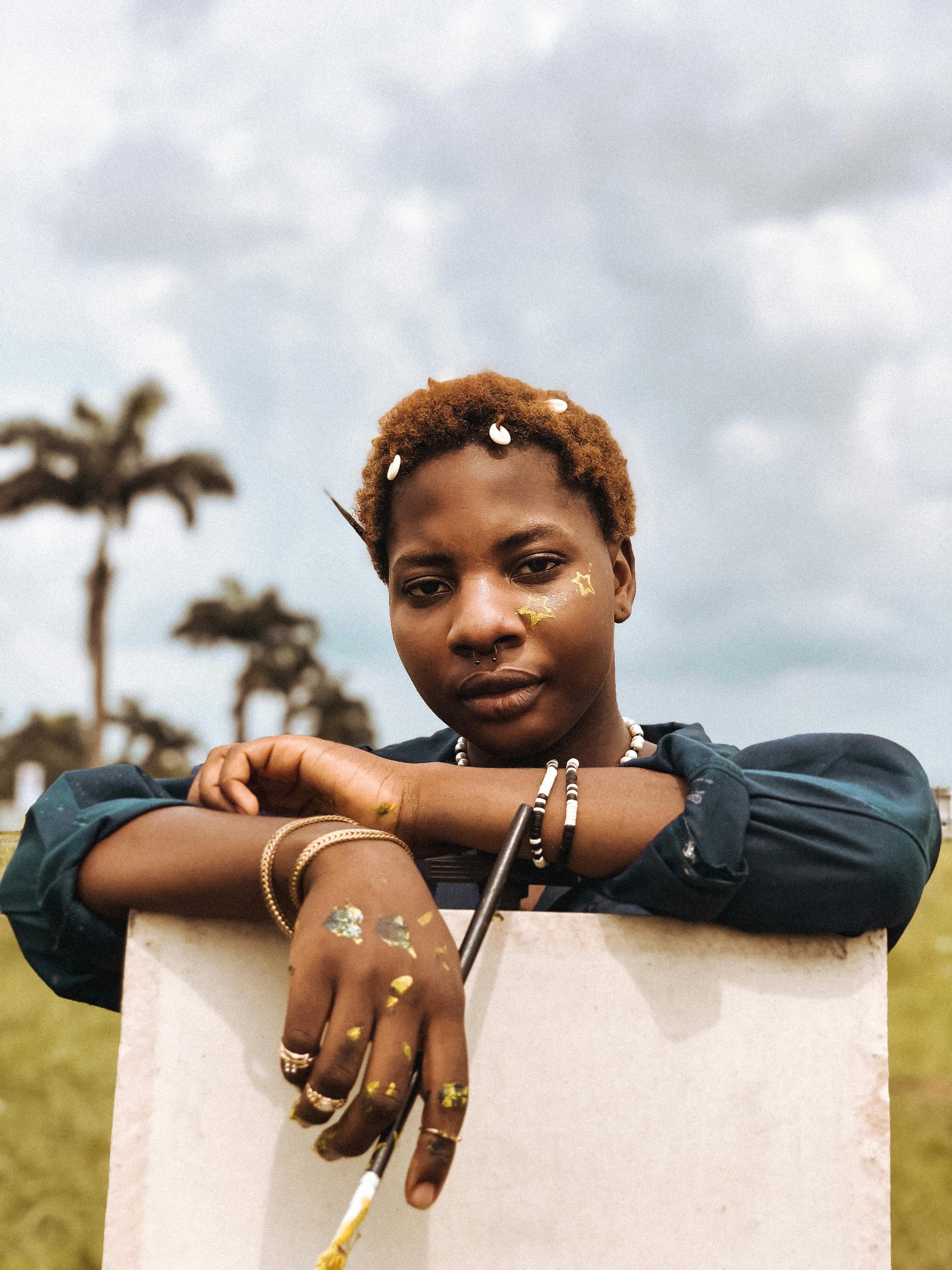Captivating portrait of a young woman with natural hairstyle leaning on an easel outdoors.