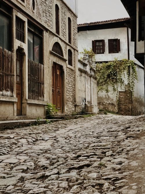 Free Rustic cobblestone street lined with vintage stone buildings in a serene historic town setting. Stock Photo