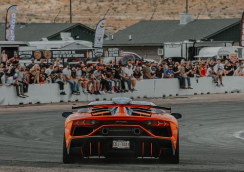 Free A stunning orange Lamborghini Aventador speeds at a race track with spectators in the background. Stock Photo