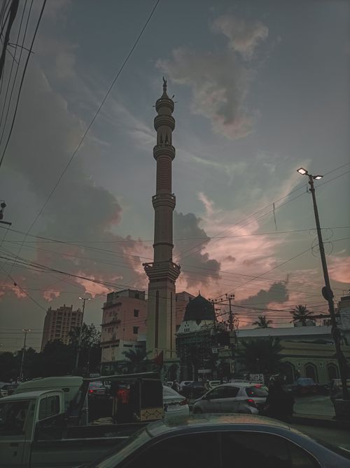 Free A beautiful sunset over a busy Karachi intersection featuring a tall mosque minaret and vibrant sky. Stock Photo