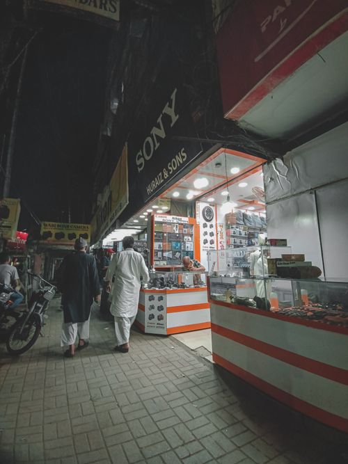Free Vibrant nighttime street scene with people walking past electronics shops and displays. Stock Photo
