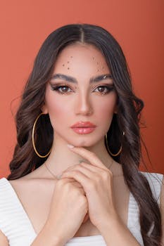 Stylish fashion portrait of a woman with makeup and hoop earrings against an orange backdrop.
