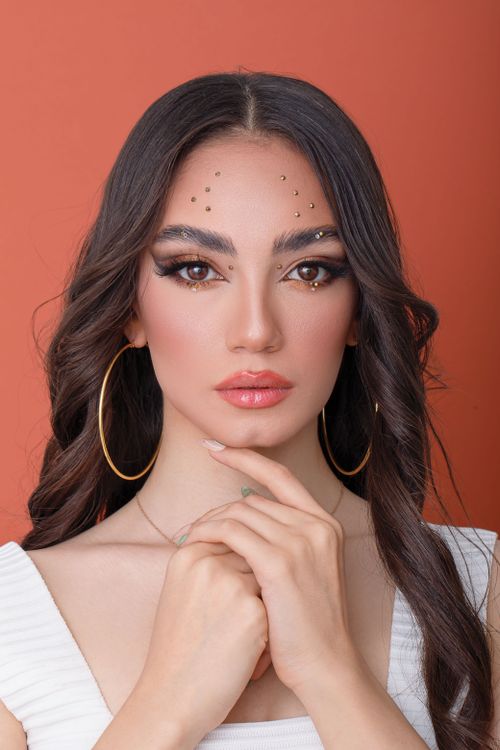 Free Stylish fashion portrait of a woman with makeup and hoop earrings against an orange backdrop. Stock Photo