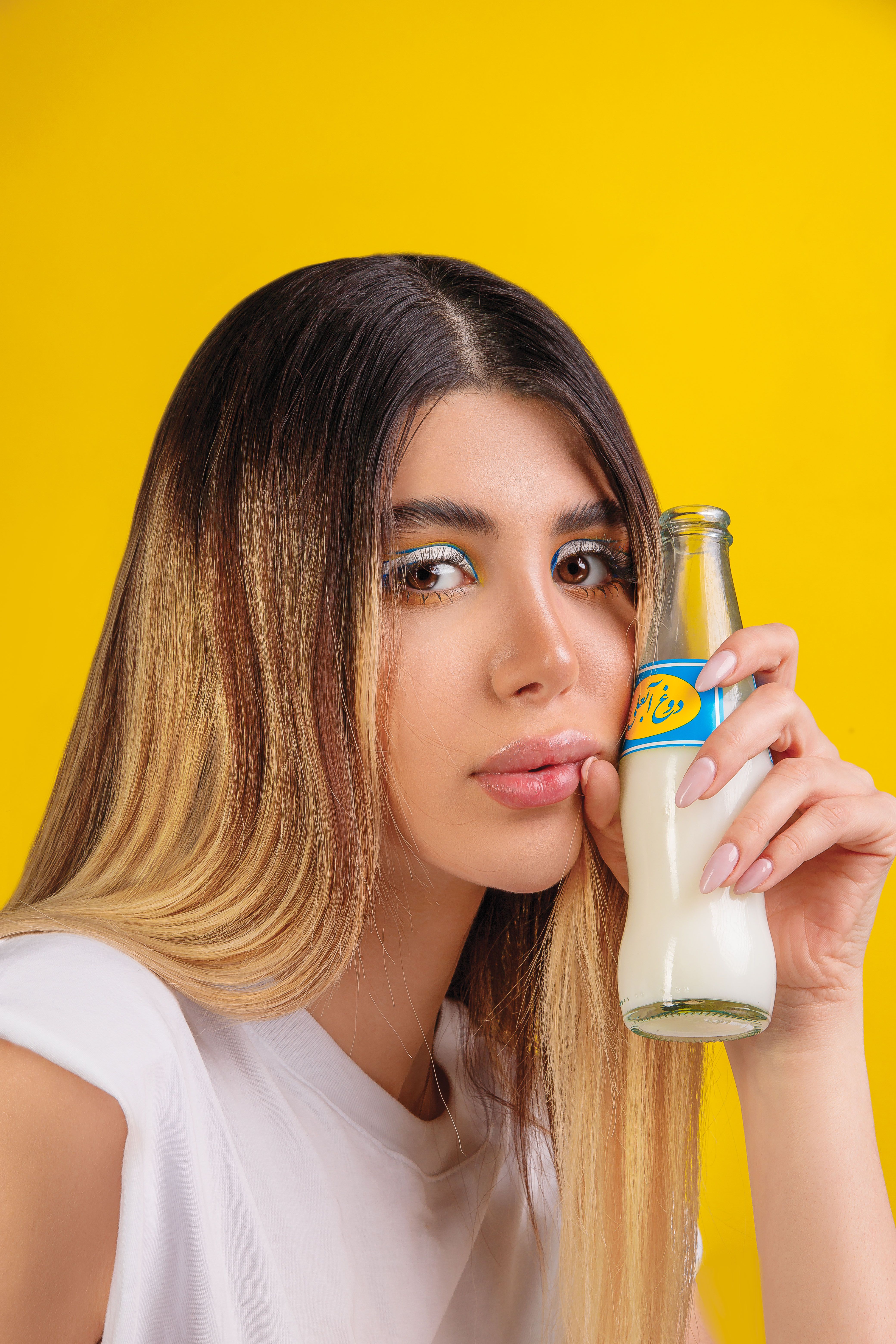 Portrait of a woman holding a bottle of milk with a vibrant yellow backdrop, showcasing modern style.