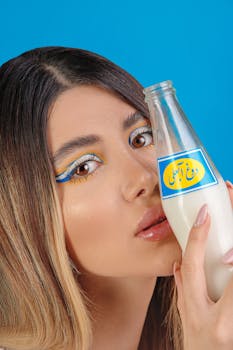 Modern portrait of a woman with artistic makeup holding a milk bottle against a blue background.