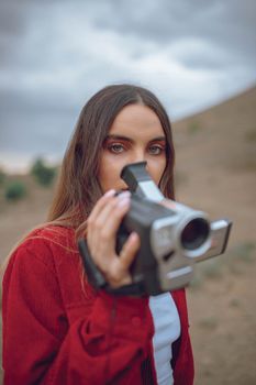 Portrait of a young woman holding a vintage camera in an outdoors setting.