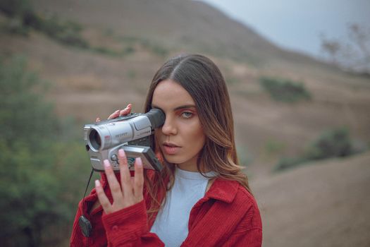 A young woman with a vintage camcorder captures video in a scenic outdoor setting.
