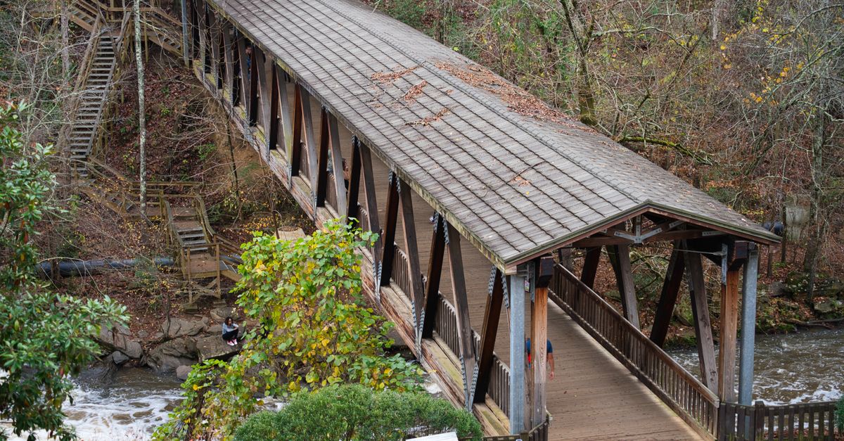 Scenic view of a historic covered bridge at Roswell Mill, GA, surrounded by autumn foliage.