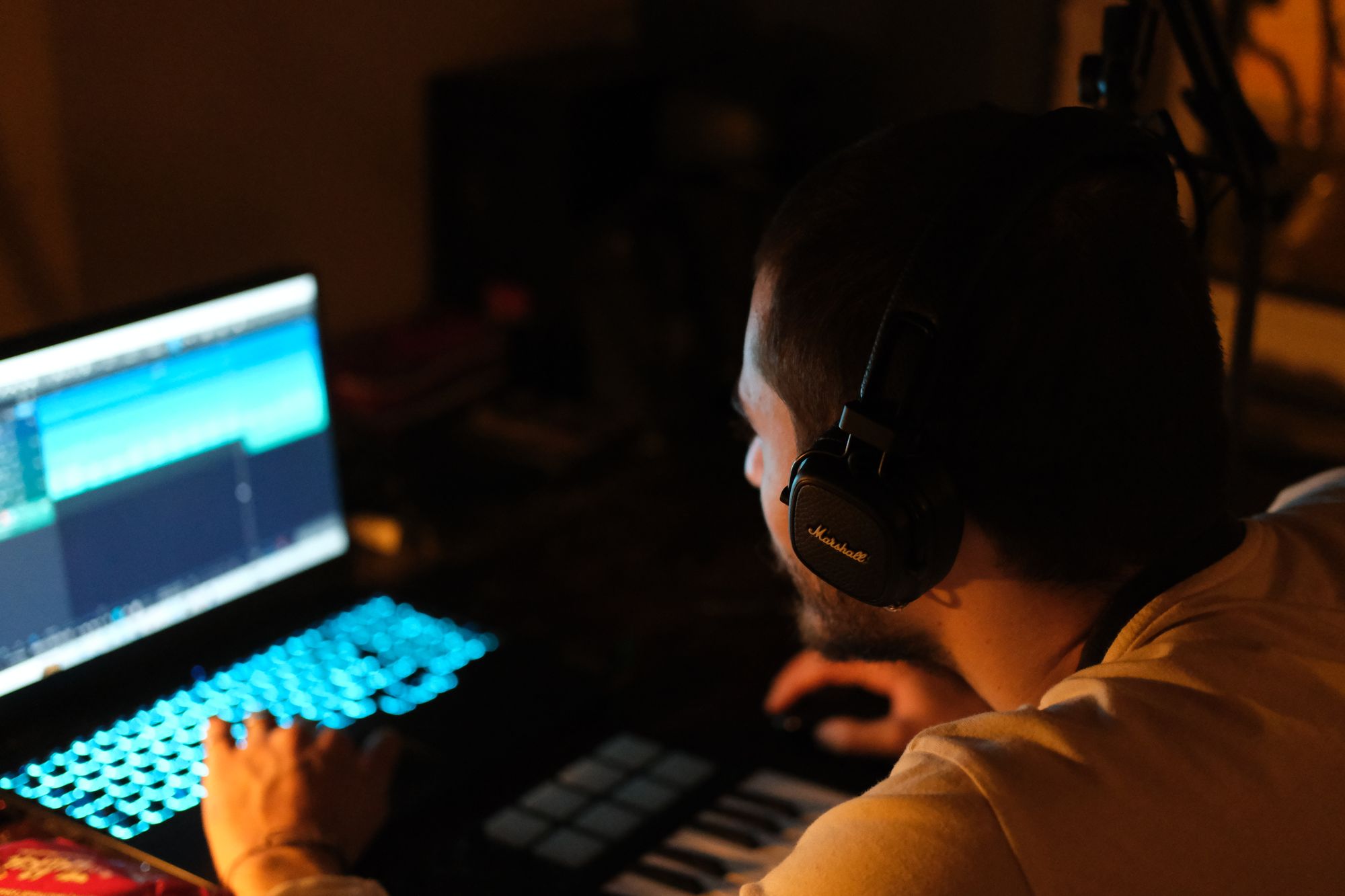 Persona con audífonos frente a una laptop en un estudio de música con luz tenue