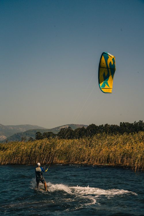 Free A kiteboarder enjoys an adventurous ride on a tranquil lake with distant mountains. Stock Photo
