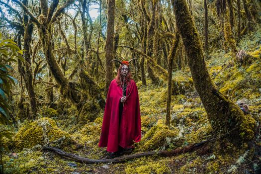 Mystical figure in a red cloak with horns standing in the lush forest of Choachí, Colombia.