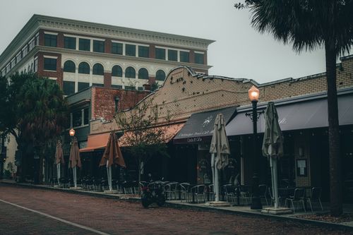 Free A charming outdoor sidewalk café in the city on an overcast day, featuring empty tables and vintage architecture. Stock Photo