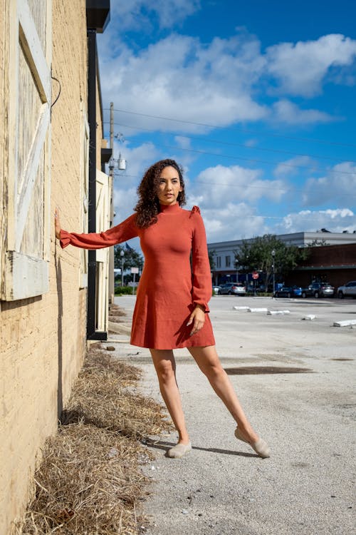 Woman in Long Sleeve Dress Standing Beside the Beige Brick Wall 