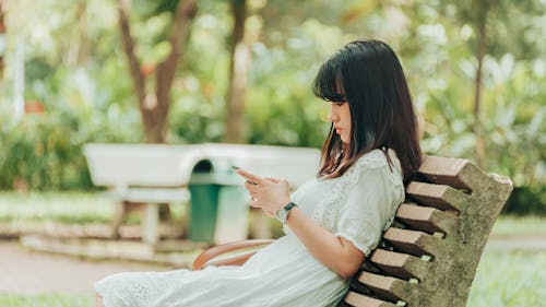 女人坐在长椅上，使用智能手机