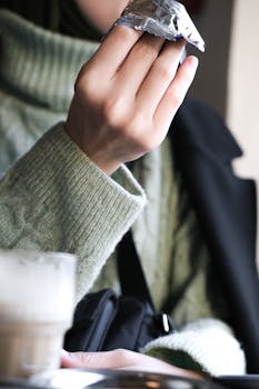 Close-up of a hand holding a wrapped snack in a cozy café setting.