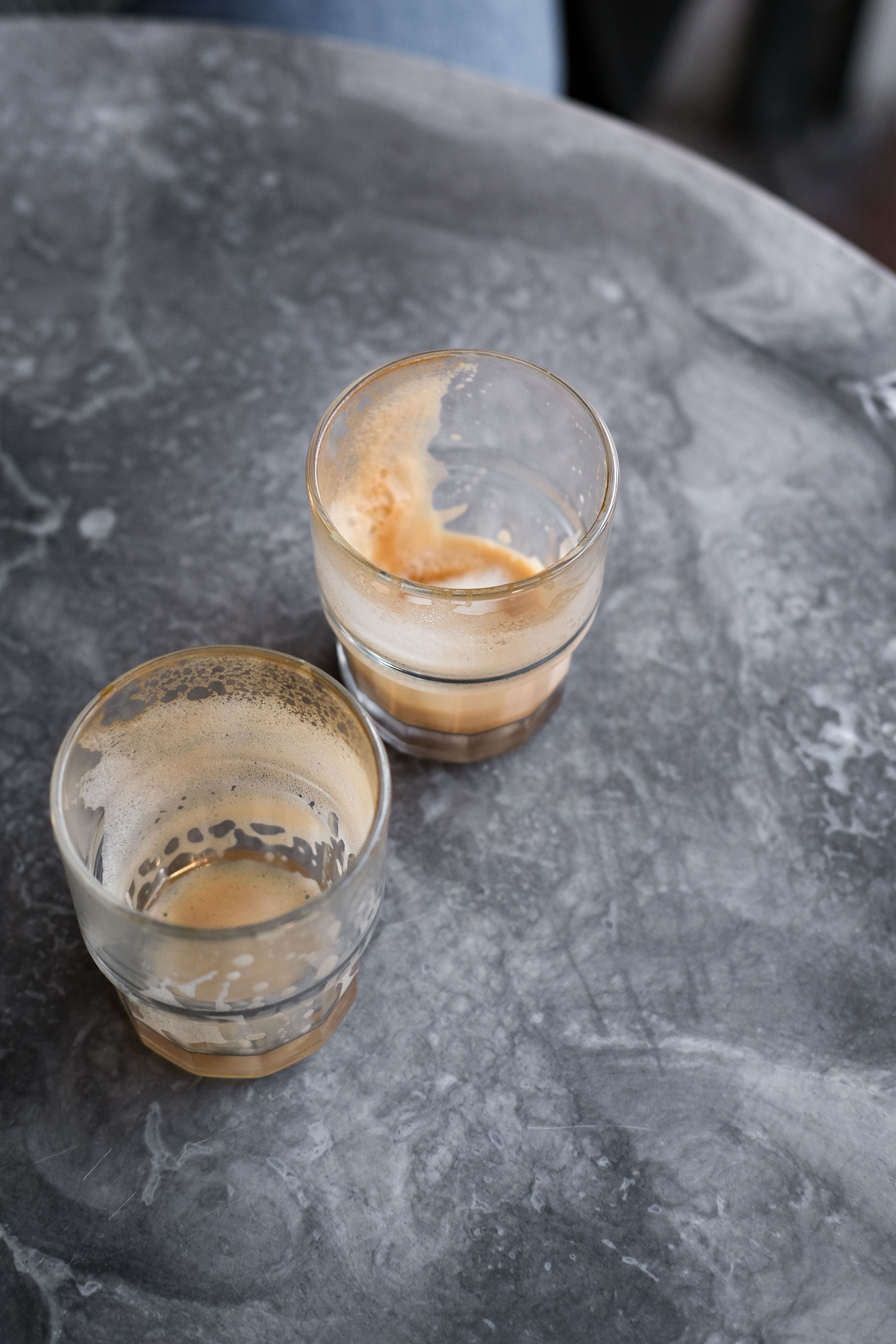 Two empty espresso glasses with foam residue on a marble table in Istanbul.