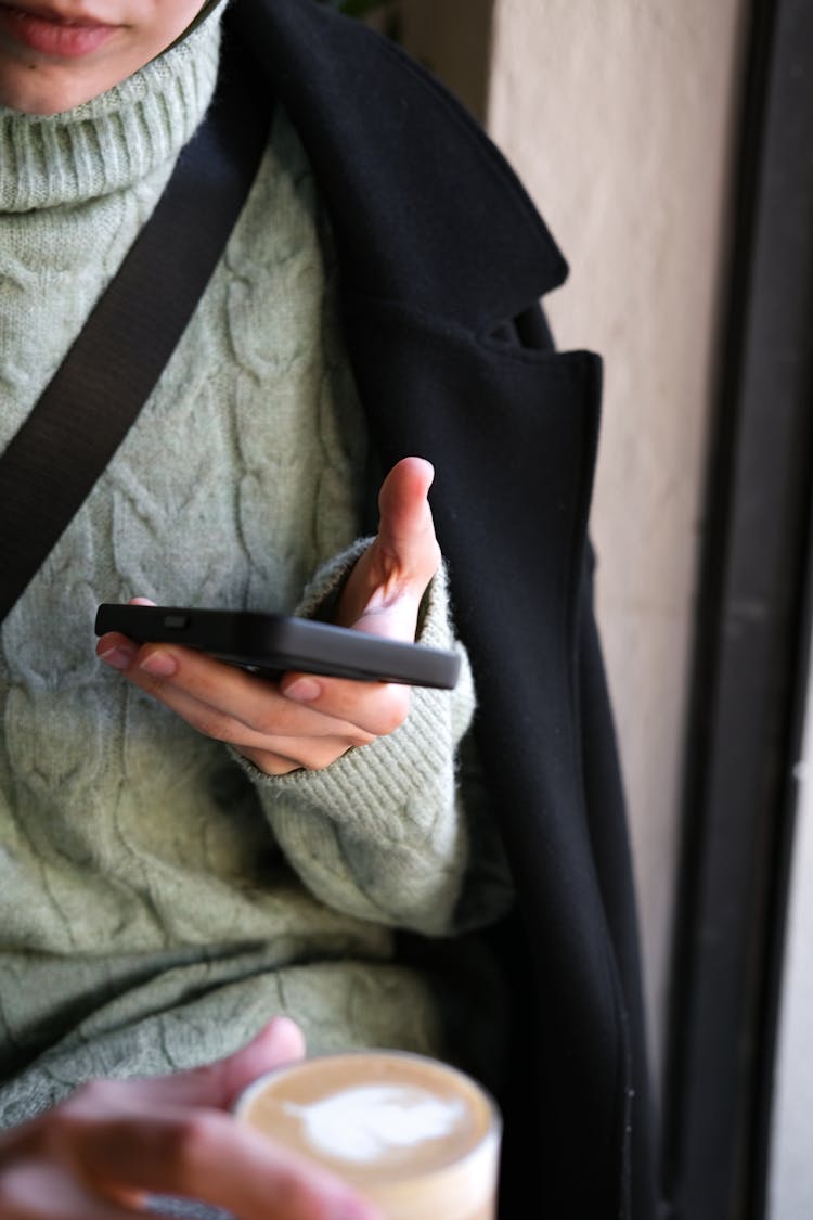 A Person In Knitted Sweater And Black Coat Holding A Phone