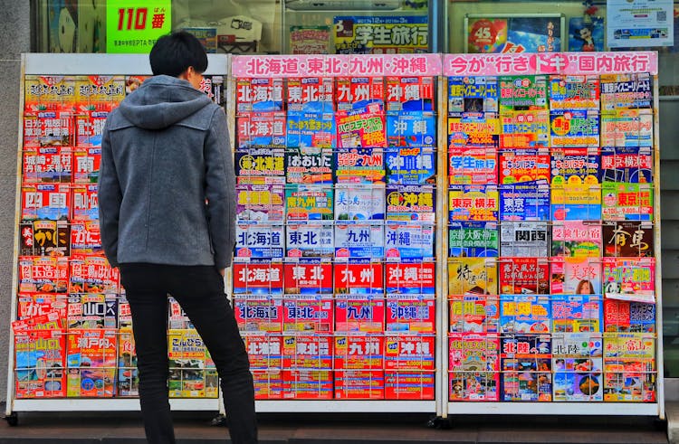 Standing Man Wearing Gray Hoodie In Front Of Magazine In Rack