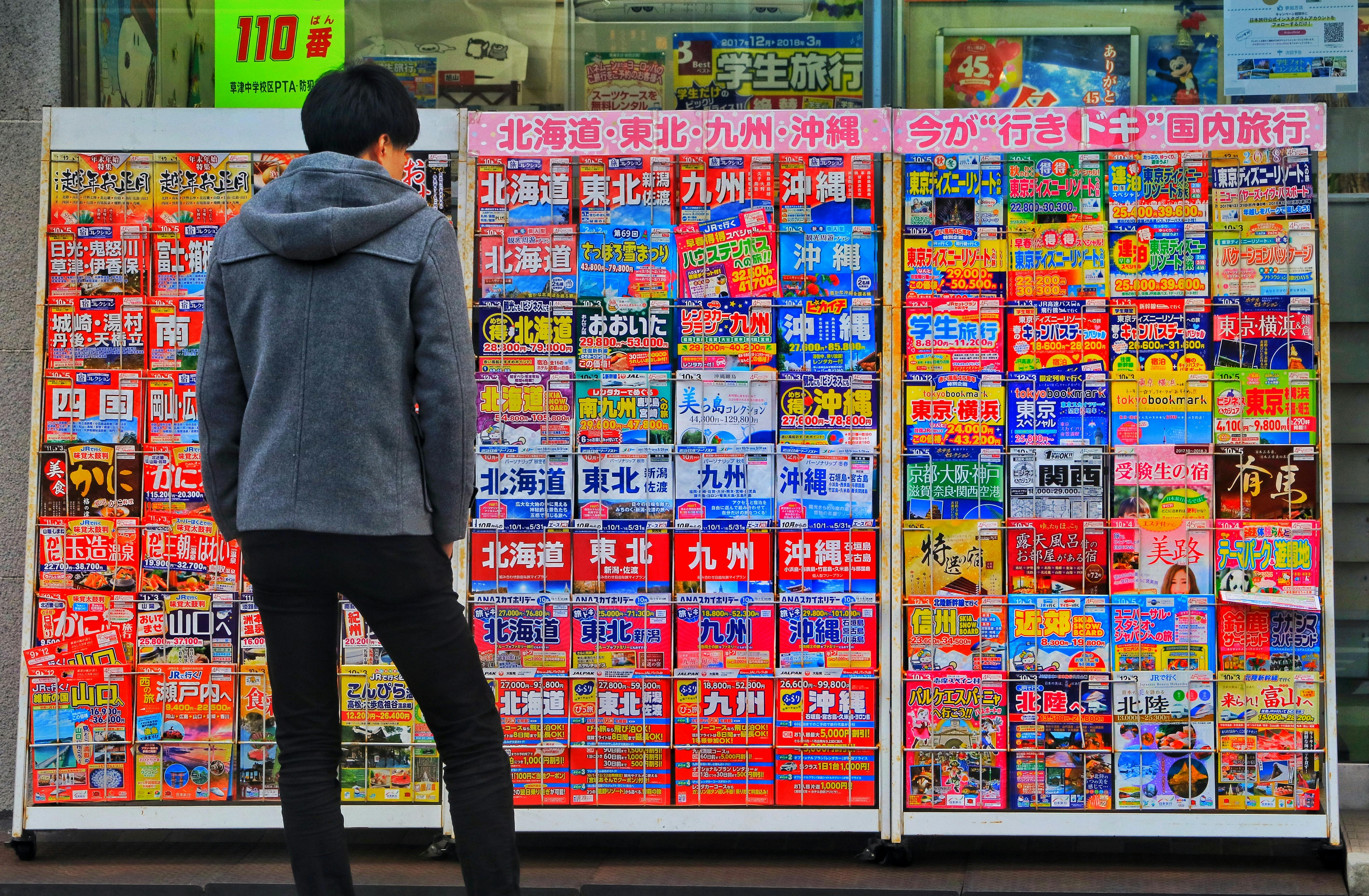 Standing Man Wearing Gray Hoodie In Front Of Magazine In Rack Free Stock Photo