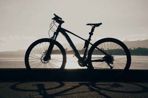 Free Silhouette of a bicycle against a tranquil lakeshore during sunset, highlighting serene travel moments. Stock Photo