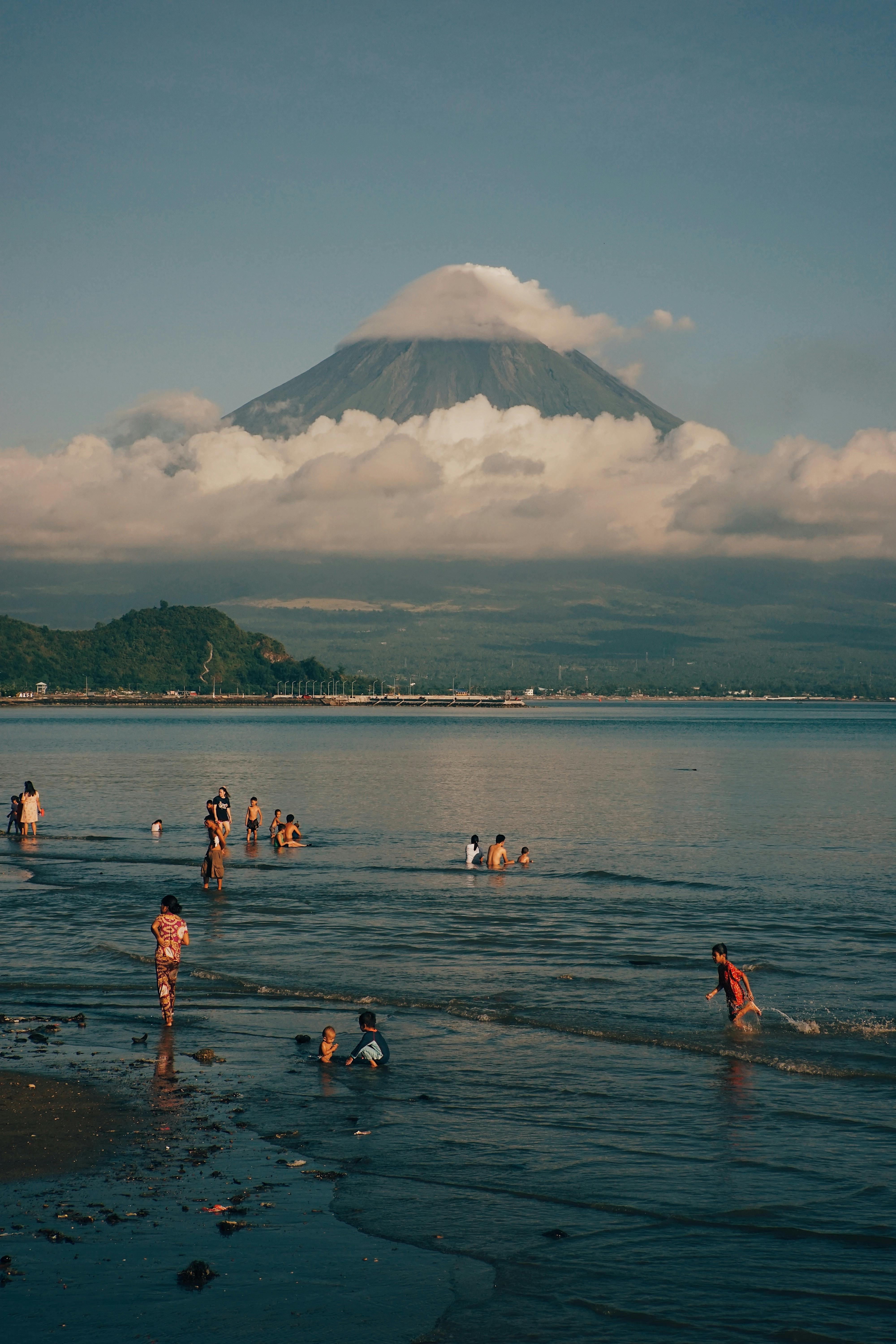 People enjoy a warm summer day at the beach with a stunning volcano view in the background.
