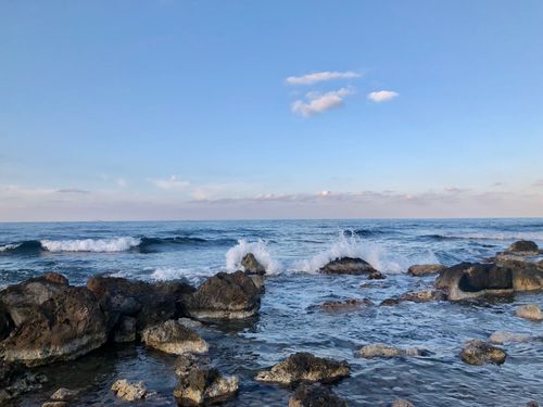 Free A serene view of waves crashing on a rocky shore under a clear blue sky at sunset. Stock Photo