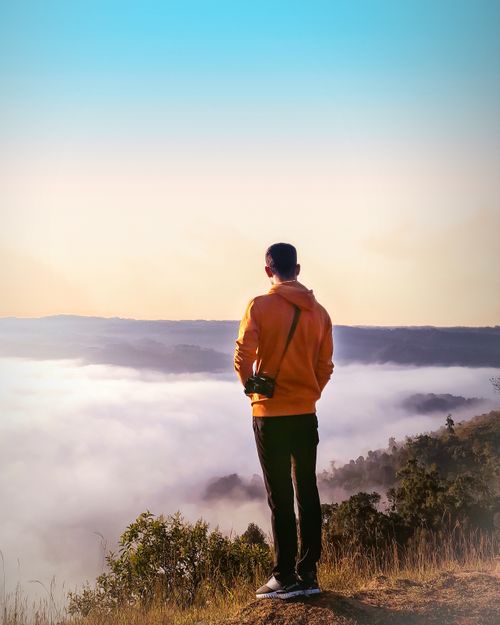 Free Man in orange jacket admires a foggy landscape from mountain top. Stock Photo