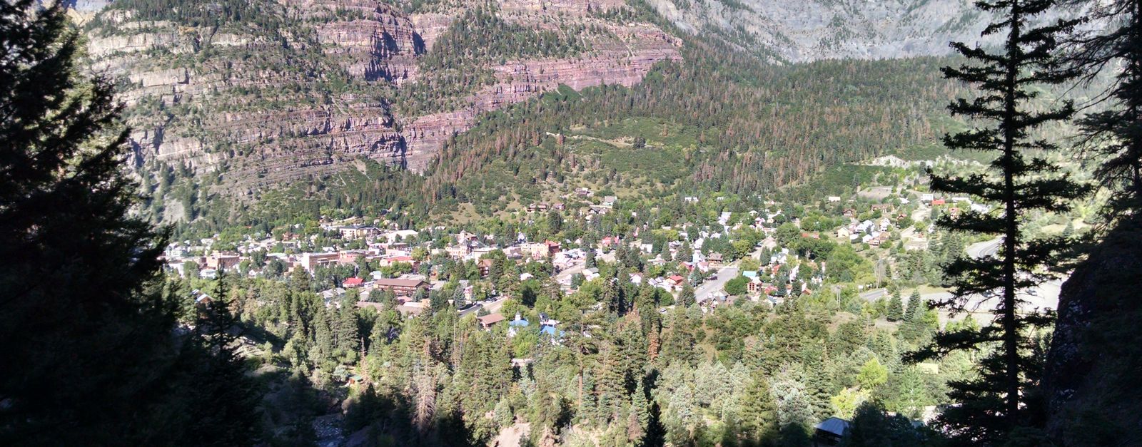 Beautiful aerial view of Ouray, Colorado surrounded by lush trees and majestic mountains under a clear sky.