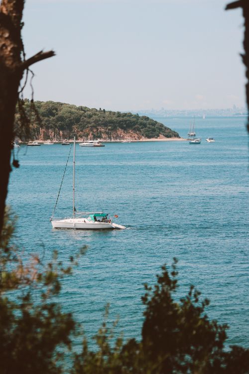 Free A peaceful scene of a sailboat on the blue sea with a lush island in the background. Stock Photo