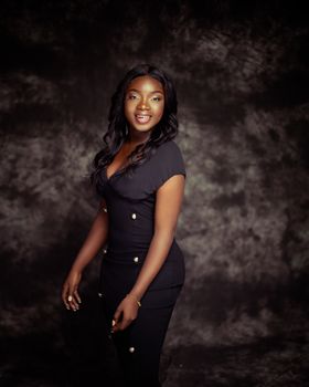 Studio portrait of a smiling African American woman in a stylish black dress, exuding confidence.