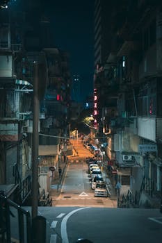 Quiet urban street at night with neon signs and parked cars creating a moody atmosphere.