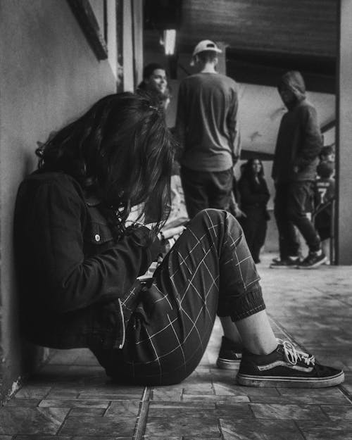 A Grayscale Photo of a Woman in Black Long Sleeves Sitting on the Street