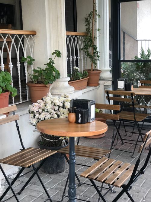 Free Charming patio setting featuring wooden tables and chairs surrounded by potted plants. Stock Photo
