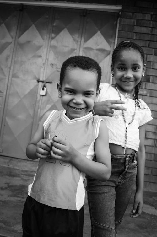 A Grayscale Photo of Young Girl and Boy Smiling while Standing Together