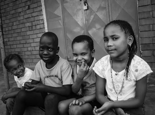 A Grayscale Photo of Young Kids Sitting on the Street