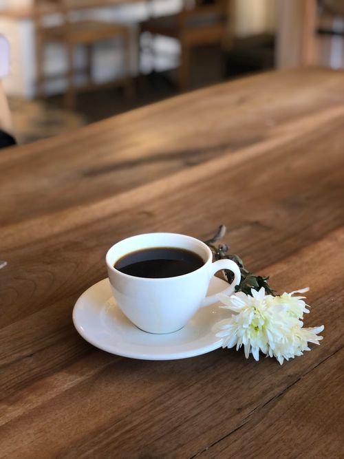 Free A white ceramic cup of coffee with a flower on a wooden table creates a peaceful, cozy atmosphere. Stock Photo