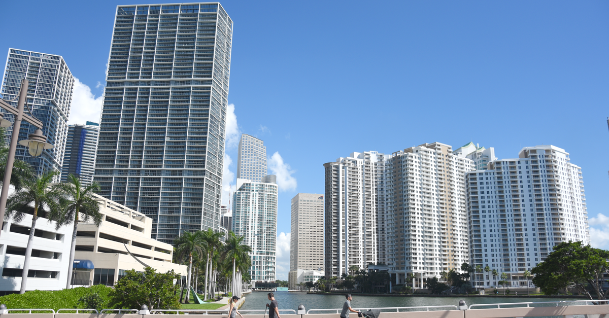 Skyline of modern skyscrapers in downtown Miami under a clear blue sky with pedestrians on a bridge.