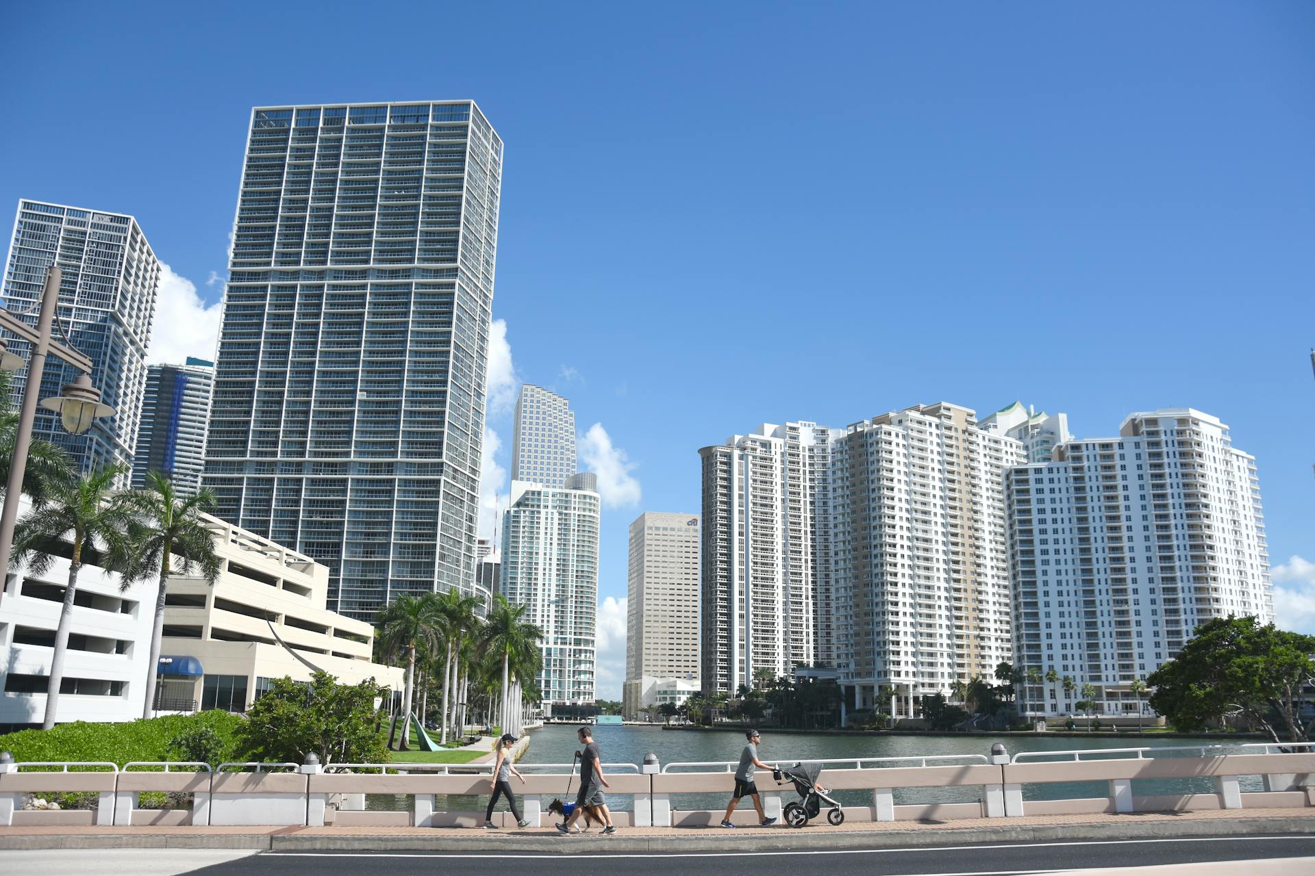 Skyline of modern skyscrapers in downtown Miami under a clear blue sky with pedestrians on a bridge.