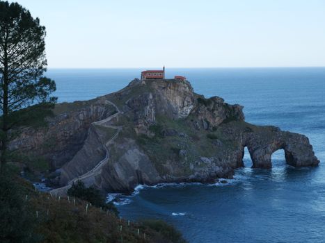 Panoramic view of Gaztelugatxe islet with chapel, arch, and pathway, surrounded by the sea.