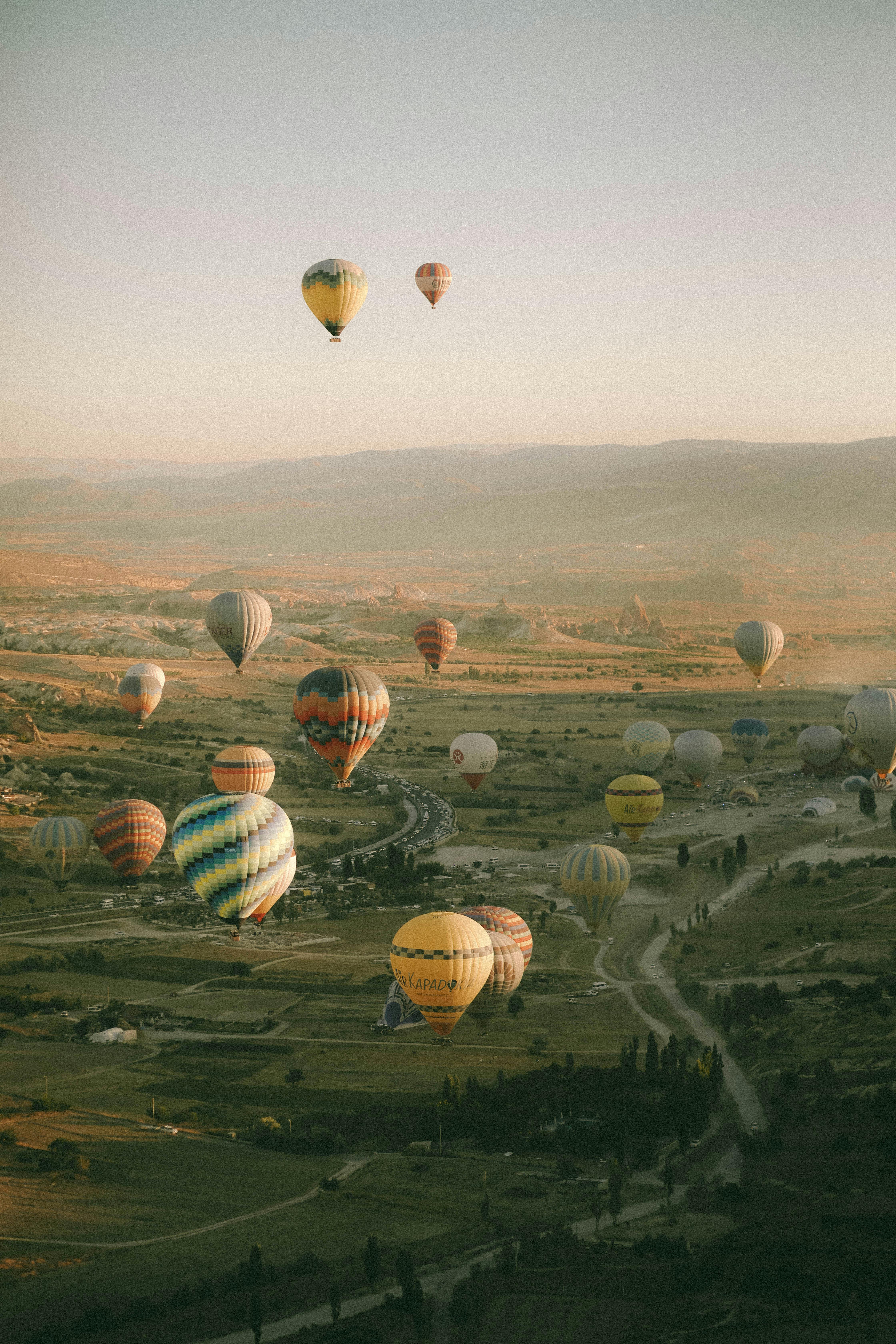 Beautiful aerial view of hot air balloons floating over Cappadocia's unique landscape at sunset.